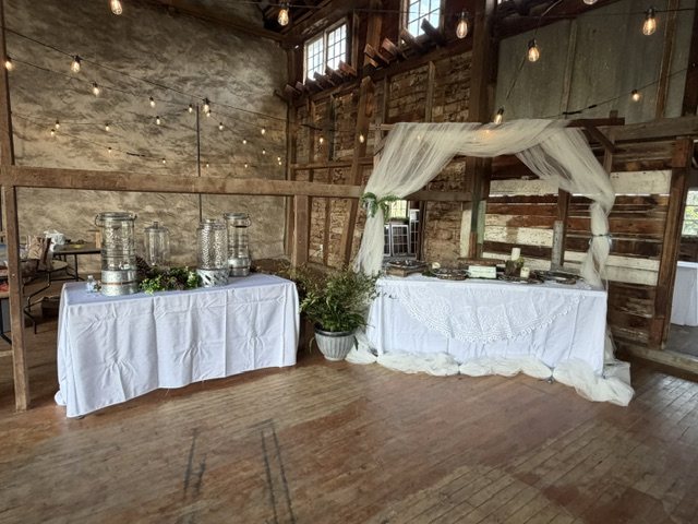 Drink station and draped arch inside the barn, under string lights