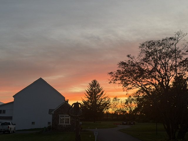 Barn and trees silhouetted against an orange sunset